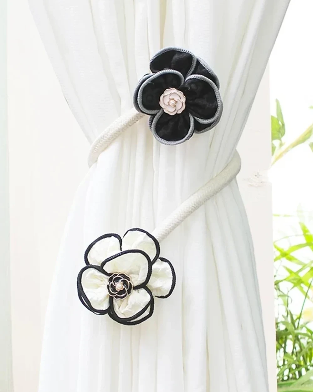 Black and ivory fabric flowers with contrasting outlines and decorative centres on a pale wrapped curtain tieback.