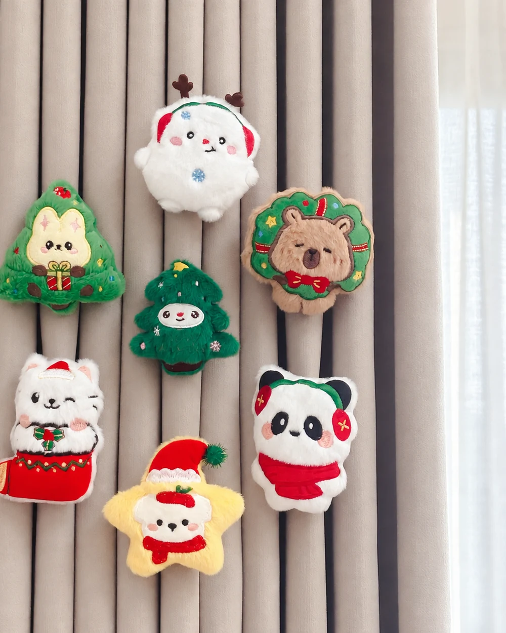Seven colourful plush festive curtain ornaments arranged across warm grey curtain folds.