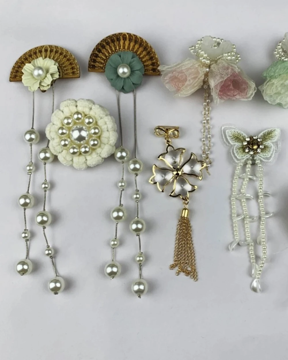 Assorted fan, flower, butterfly and pearl-look curtain ornaments in ivory, sage and gold tones.