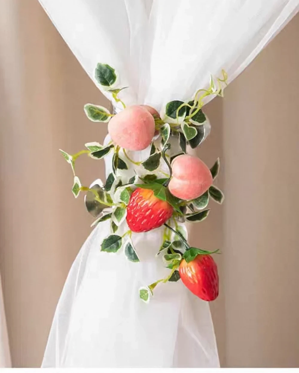 Decorative pink peaches, red strawberries and trailing green leaves gathered around a white sheer curtain.