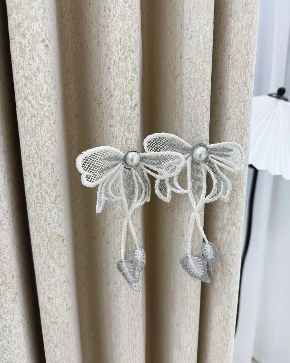 Two silver and ivory embroidered bow curtain ornaments with pearl-look centres and leaf pendants.