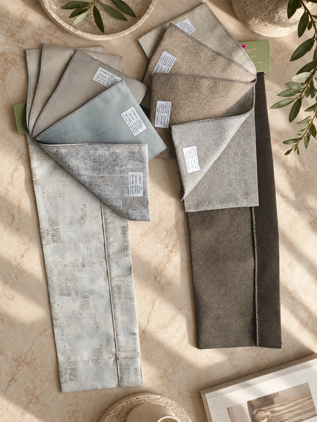 Dimout curtain fabric samples in beige, taupe, grey and pale blue, with textured woven finishes and labelled swatches arranged on a cream stone surface.