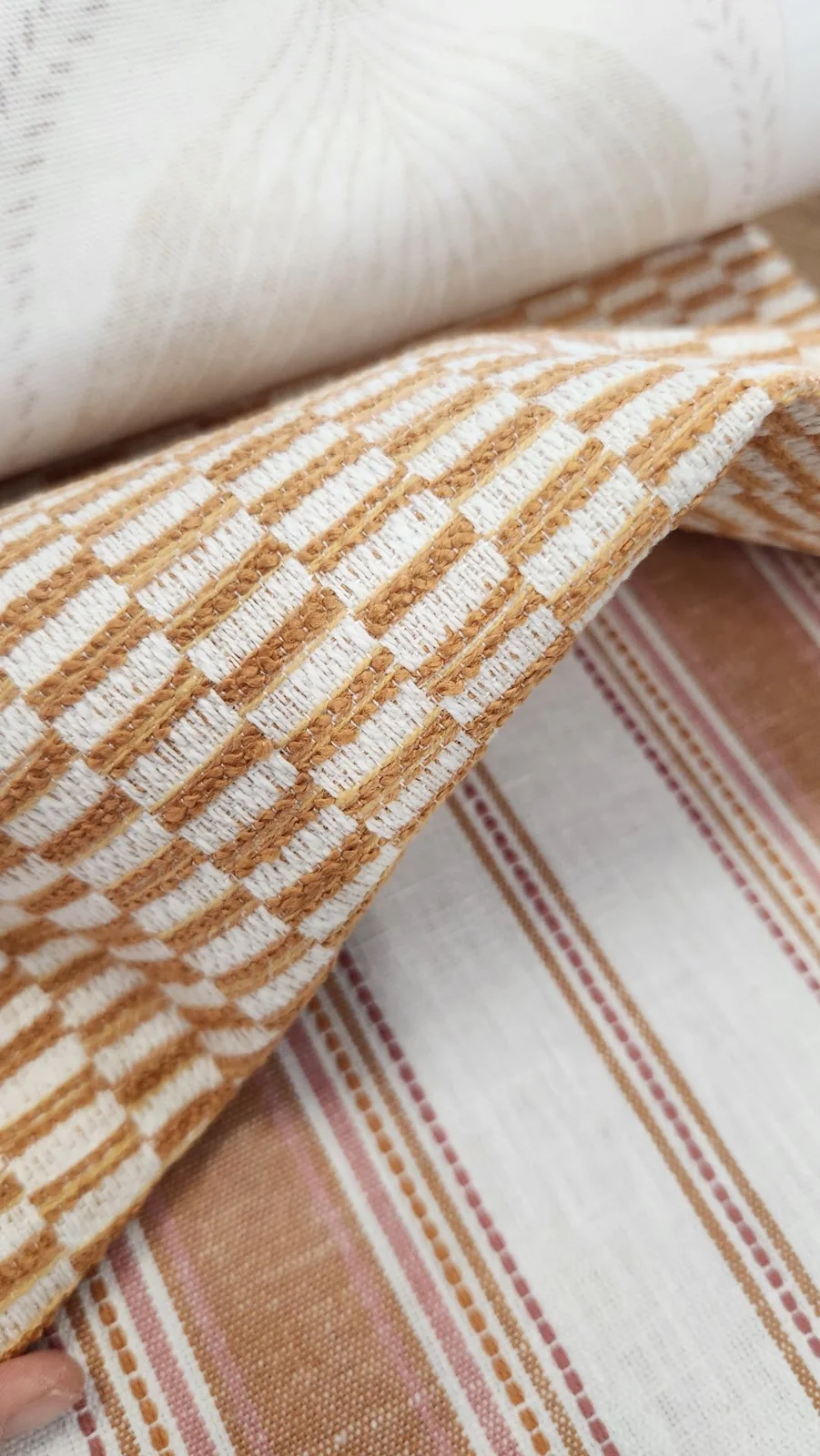 Warm ochre-and-cream basket/check weave layered over striped fabric samples.