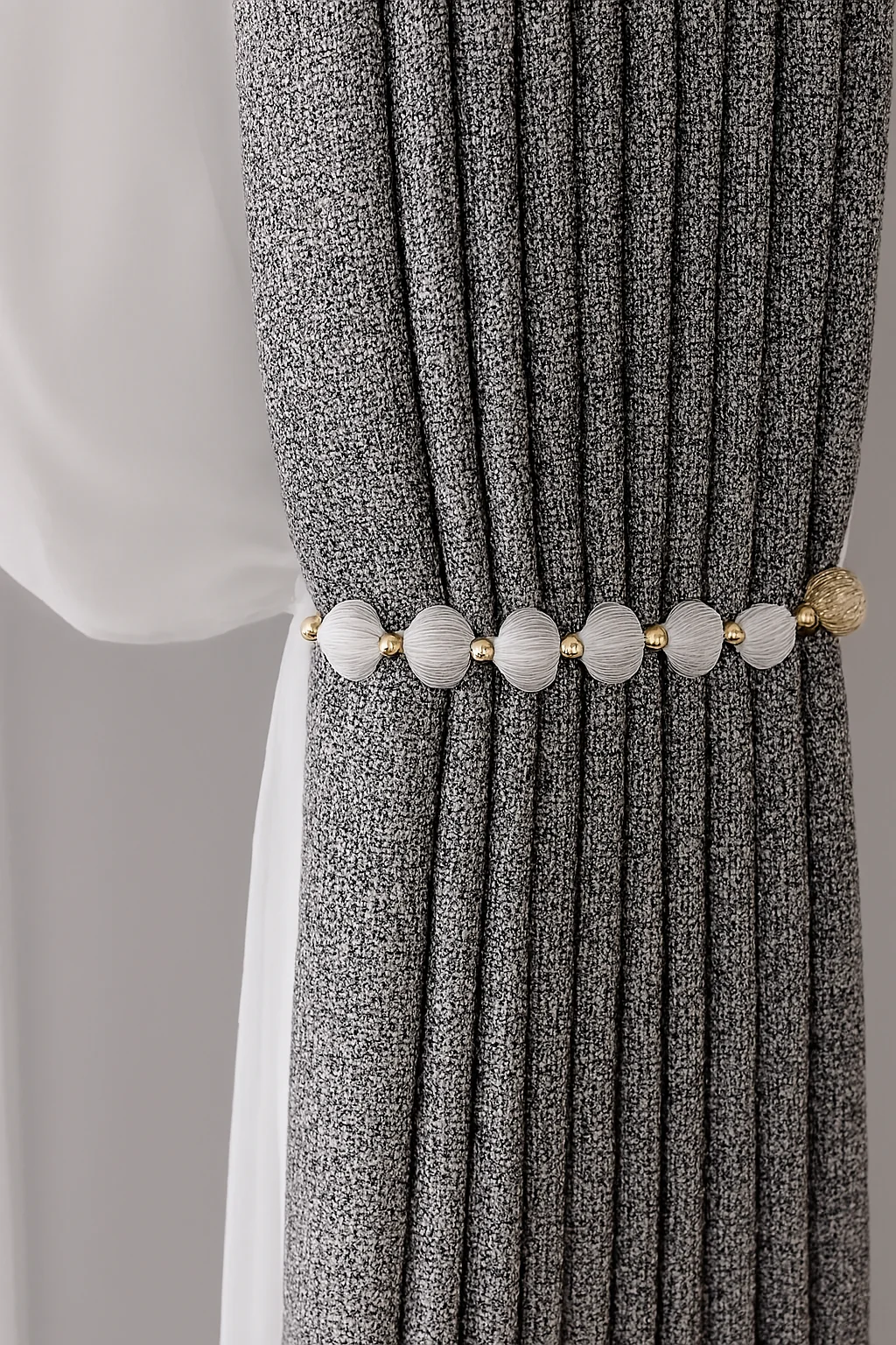 Dark charcoal finely textured curtain gathered by white stone-like disc tieback.