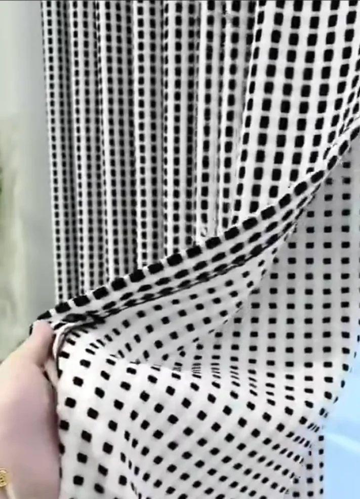 Black-and-white open grid/check patterned sheer textile held up in close-up.