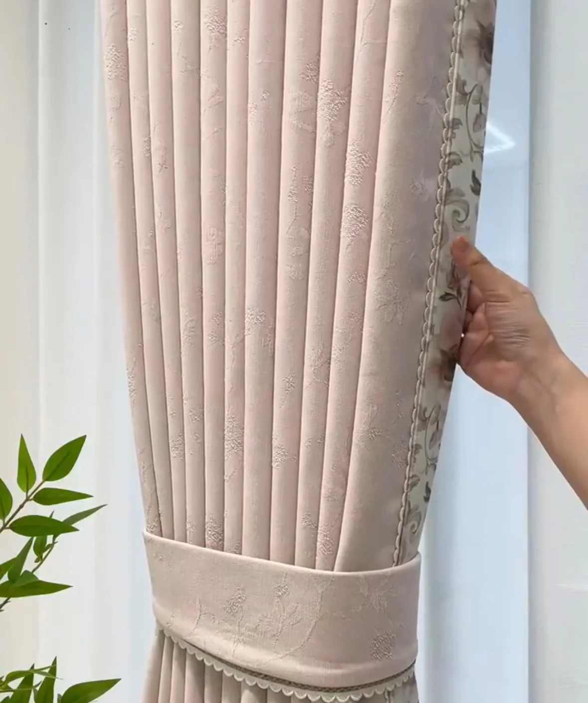 Blush-pink textured curtain with floral decorative edge trim and broad matching tieback.