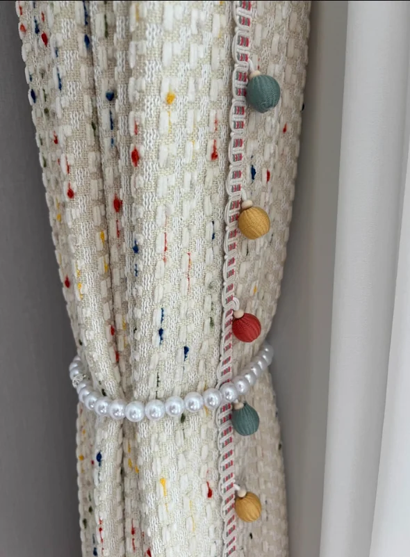 Chunky pale multicolour-flecked fabric with colourful pom-pom edge and pearl-like tieback.