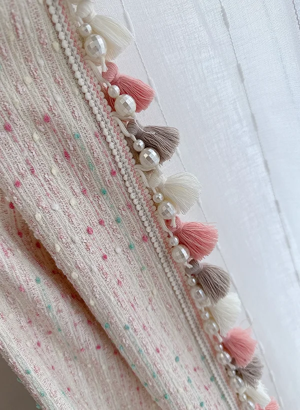 Pale textured fabric with coloured flecks and pink, ivory and taupe tassel-and-pearl trim.