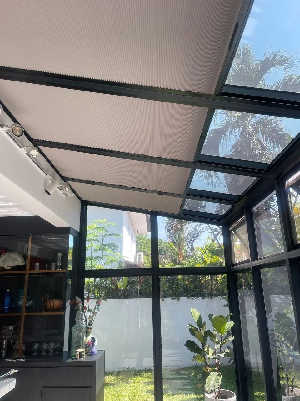 Light shade spanning the roof of a glazed conservatory/sunroom; roof tracks and uncovered edge glazing visible.