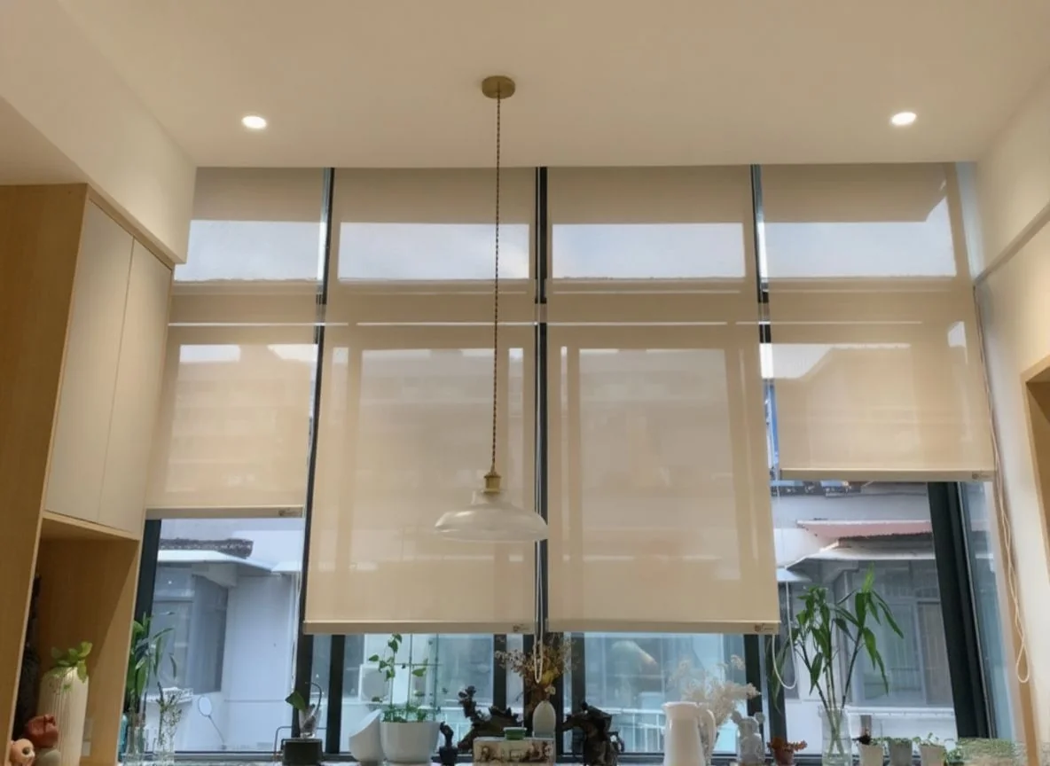 Three pale roller screens lowered partway over tall glazing in a furnished double-height interior.
