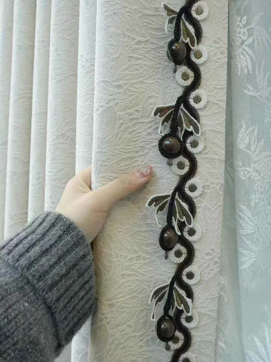 Ivory textured drape with vertical black undulating vine braid, ivory circular embroidered motifs and small dark glossy bead drops at leading edge — supplied curtain design reference.
