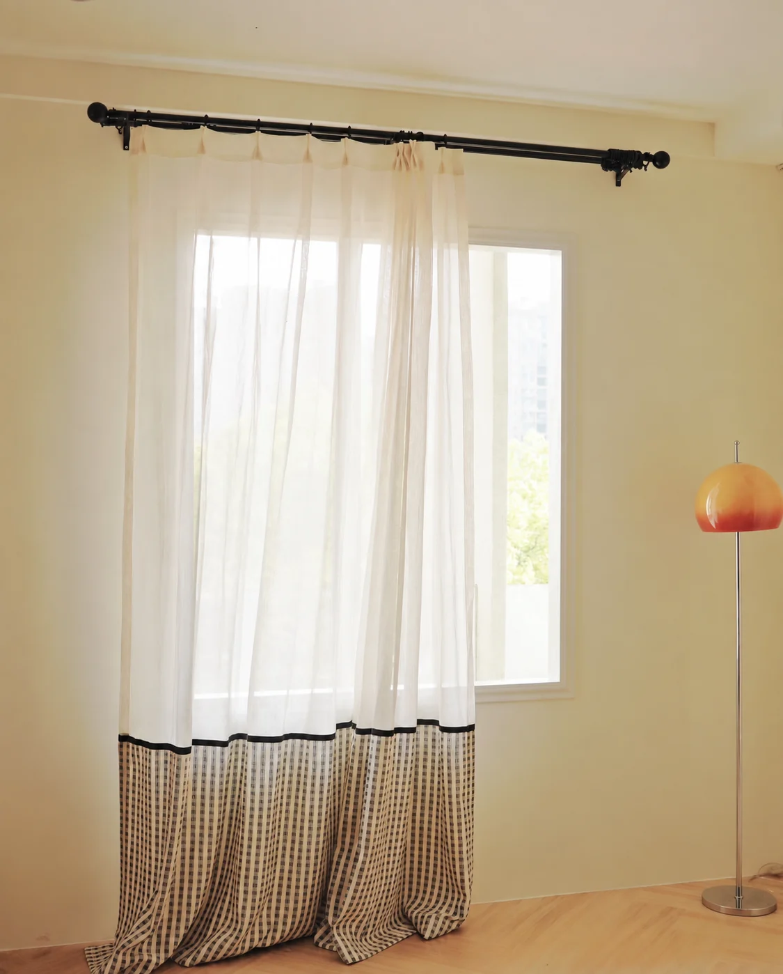 Ivory translucent upper curtain joined to taupe-black small gingham checked lower section at roughly bottom quarter, narrow black ribbon along join — supplied curtain design reference.