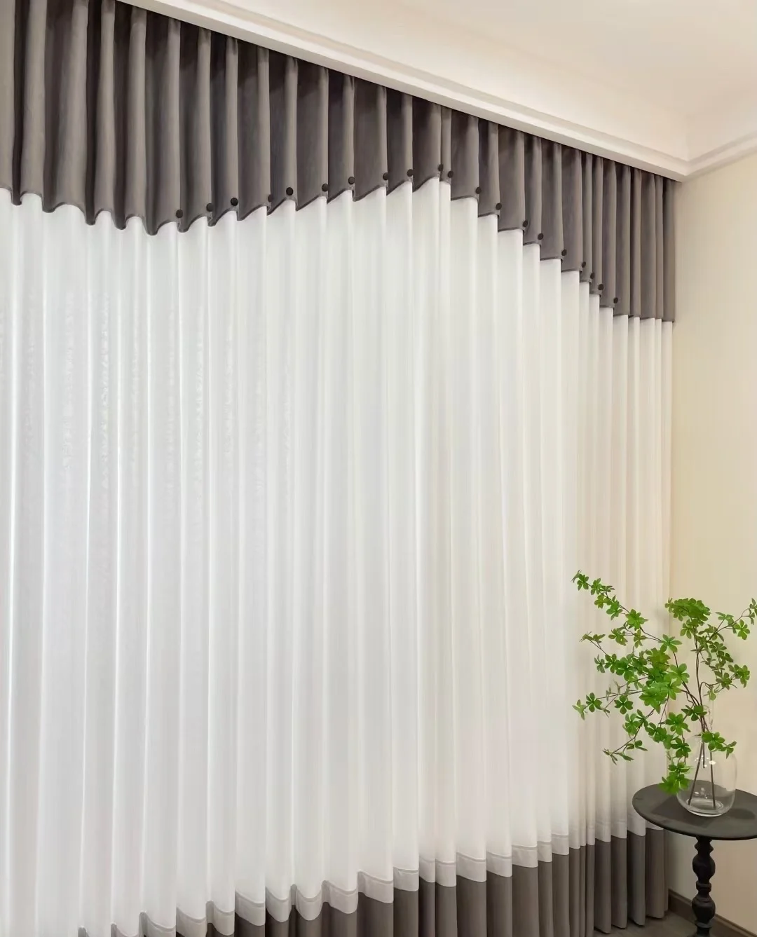 White sheer full-length curtain with grey upper shaped scalloped band and small black discs along join, matching grey lower hem band — supplied curtain design reference.
