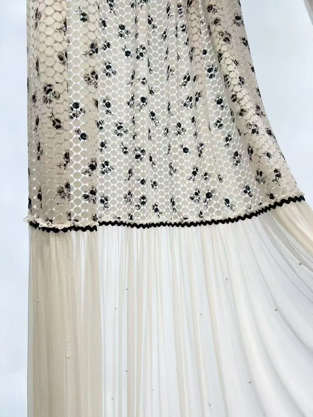 Cream open net upper panel with small black floral sprigs, black zigzag/rickrack ribbon horizontal seam above fine ivory lower sheer with tiny pearl-like dots. — supplied curtain design reference.