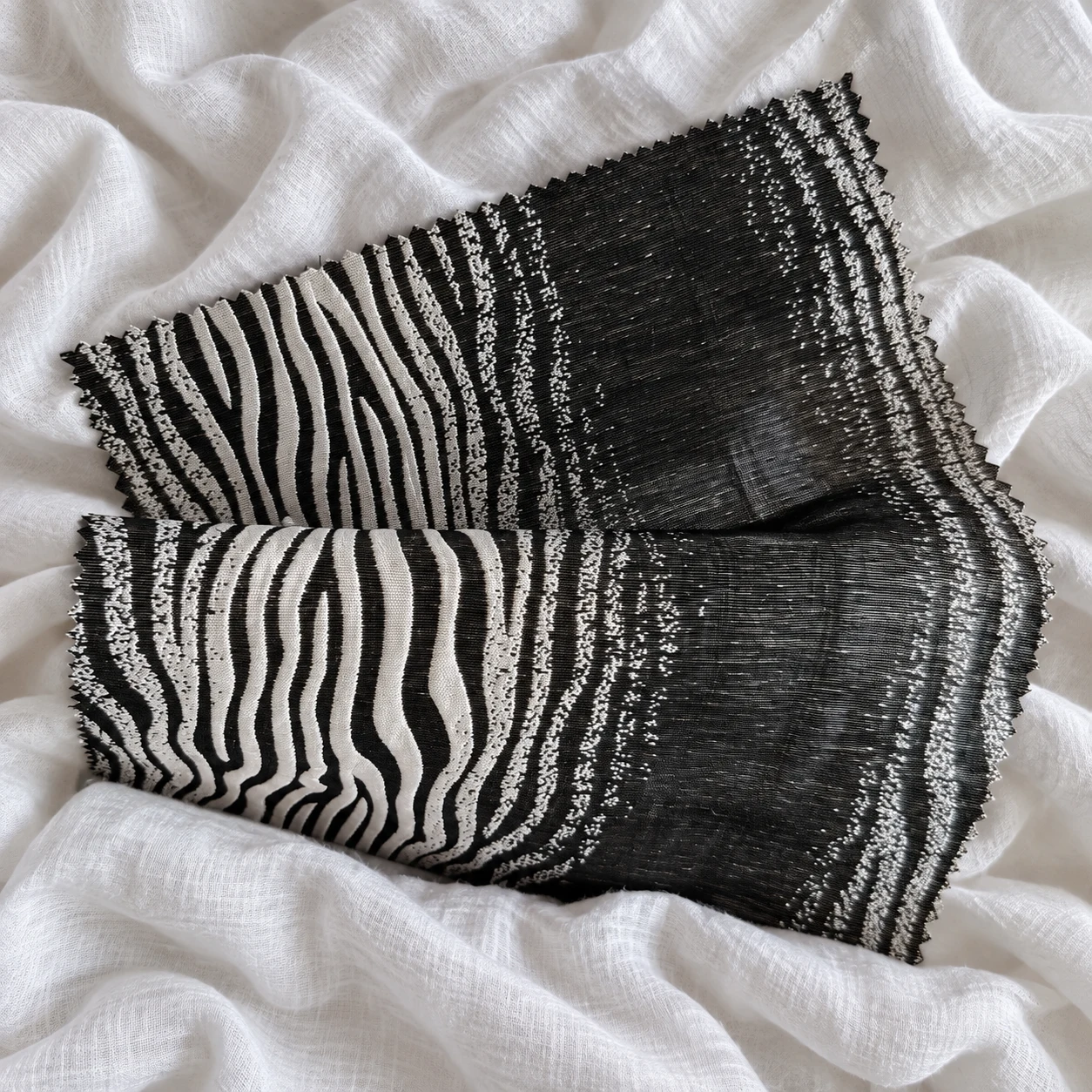Black-and-ivory zebra-pattern swatch transitioning to charcoal woven fabric, folded on white linen.