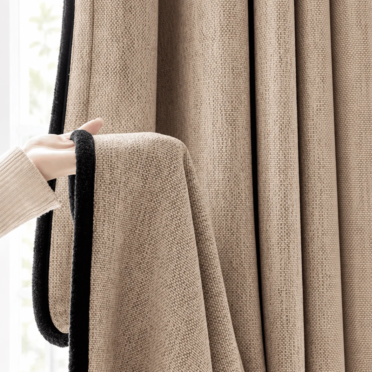 Coarse taupe curtain fabric with a black contrast edge, held against matching hanging drapes.