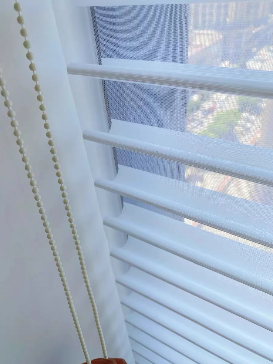 Close view of soft white horizontal vanes extending between two sheer faces, with open passages and side control chain.